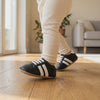 Un bebé camina con los zapatos negros de rayas blancas