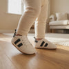 Un bebé camina con los zapatos blancos de rayas negras