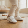 Un bebé camina con los zapatos blancos con velcro